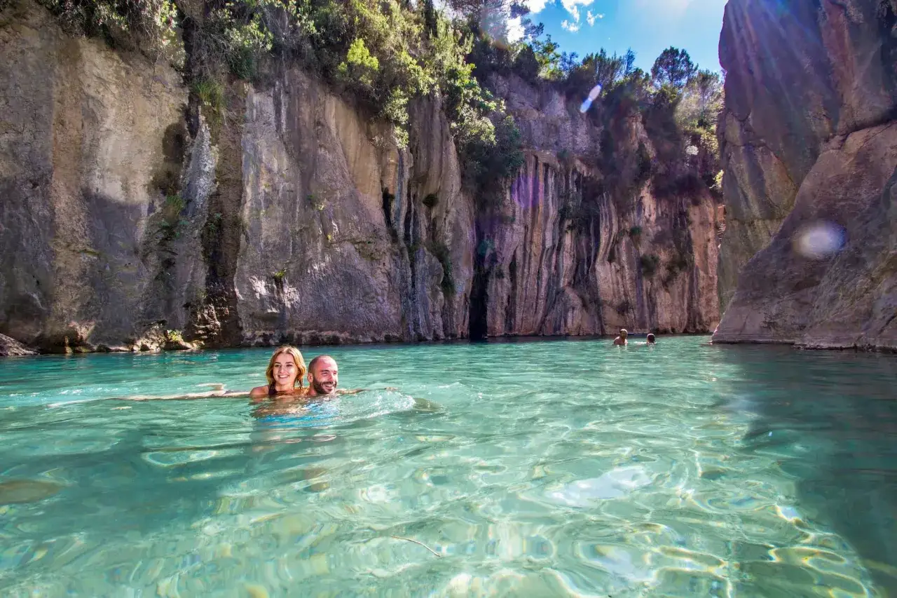 Pareja disfrutando del agua cristalina en el balneario de Montanejos, rodeados de imponentes paredes rocosas y vegetación.