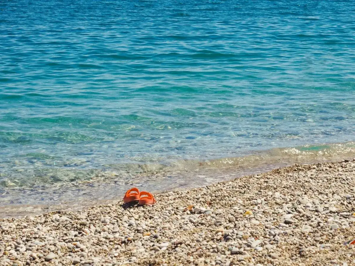 Chanclas naranjas abandonadas en la playa Malvarrosa de Corinto, esperando a su dueño junto a las aguas cristalinas.