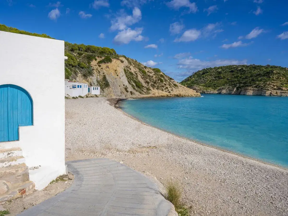 La cala Barraca con sus aguas turquesas y casitas blancas, un refugio idílico bajo el sol.
