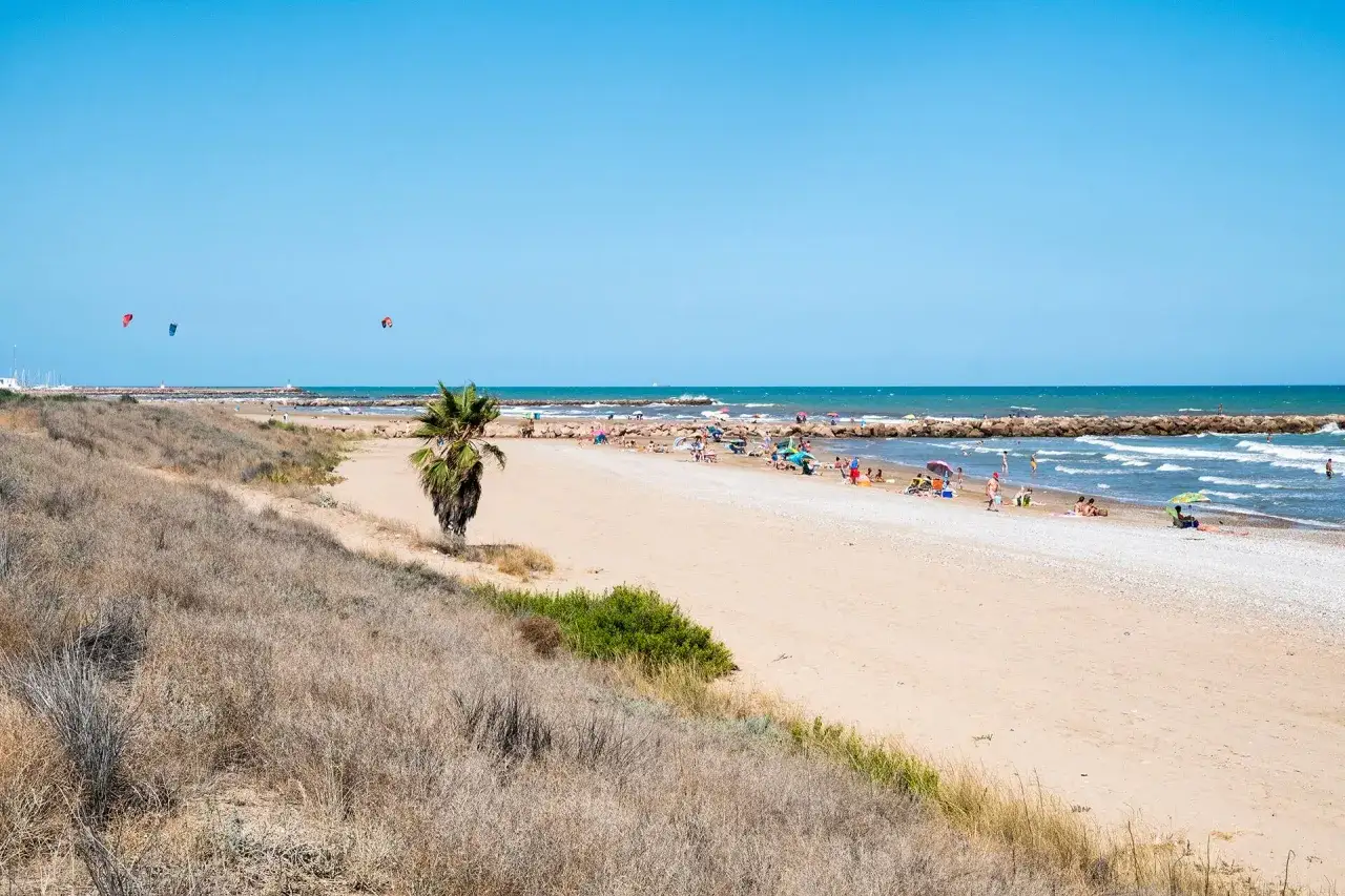 Gente disfrutando del sol y el mar en la playa de Massamagrell. Kitesurfistas navegan en el horizonte.