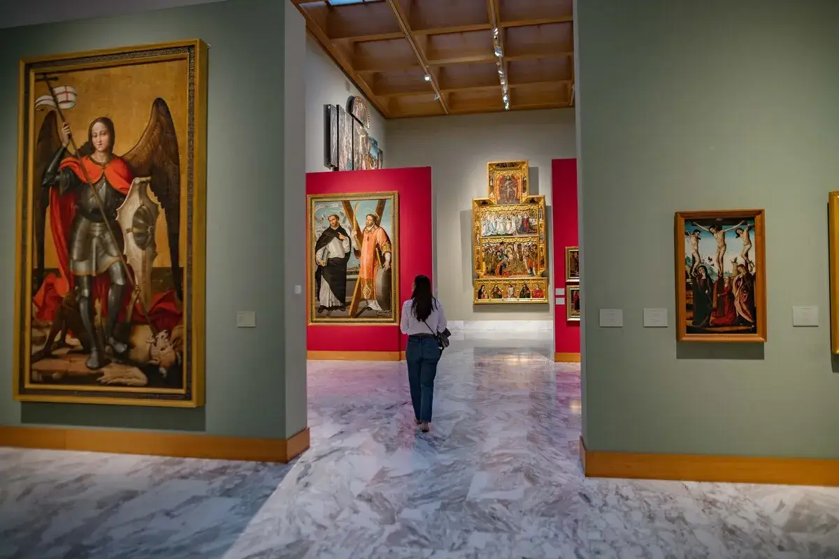 Una mujer camina por una sala del museo de bellas artes valencia, admirando pinturas religiosas.