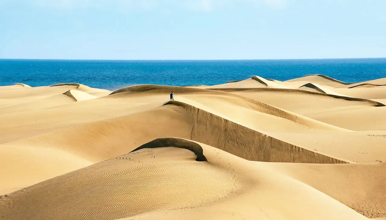 Un explorador solitario en la playa Moncayo, rodeado de dunas doradas y el mar azul.