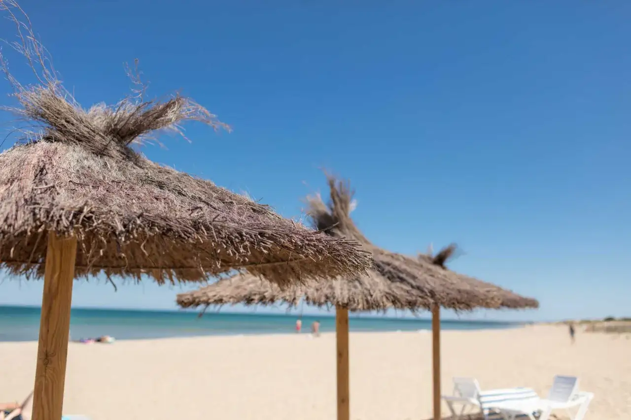 Sombrillas de paja en la playa Carabassi, con el mar azul y el cielo despejado de fondo.