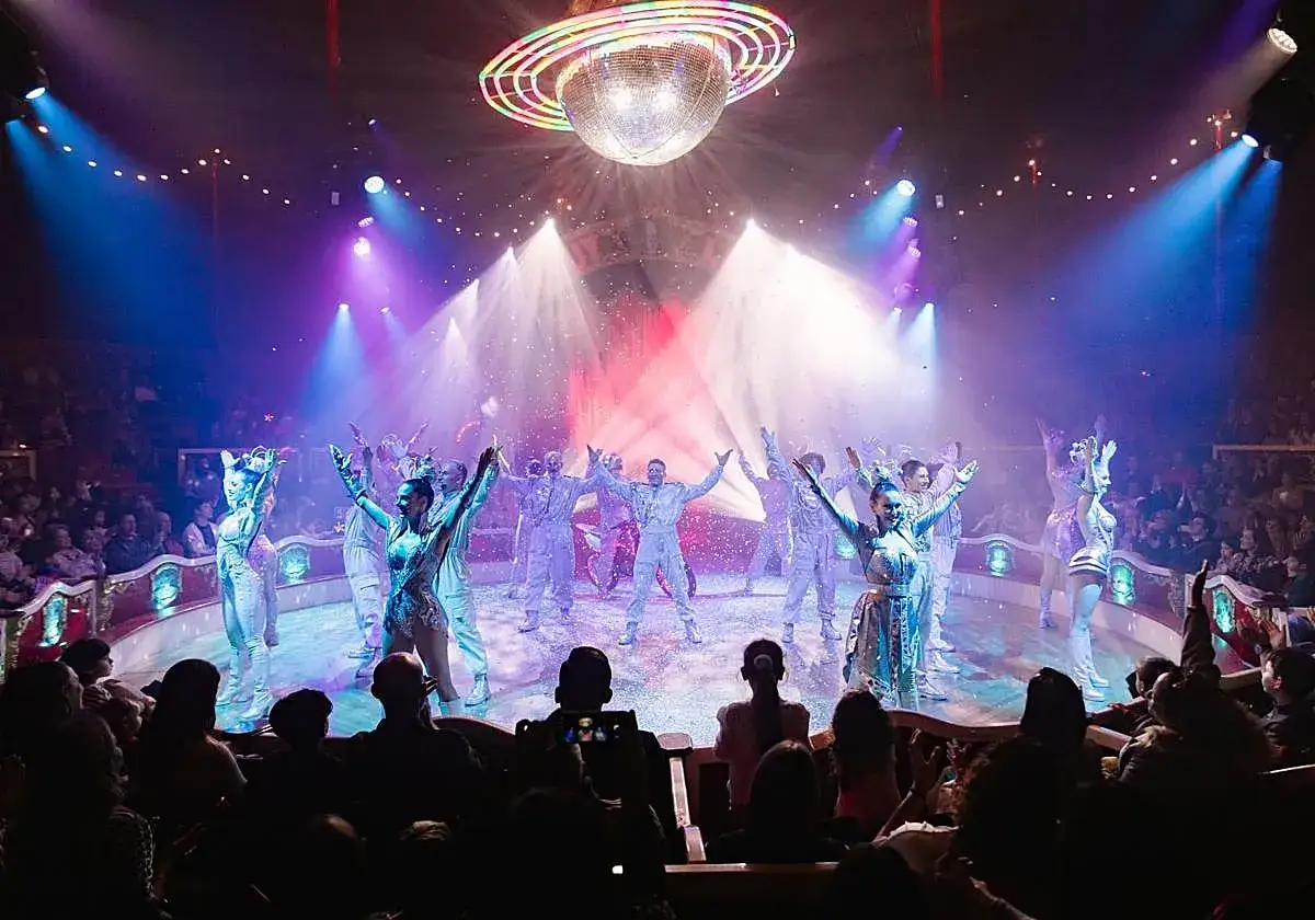 Elenco del circo Raluy Alicante saluta il pubblico sotto una palla da discoteca e luci colorate.