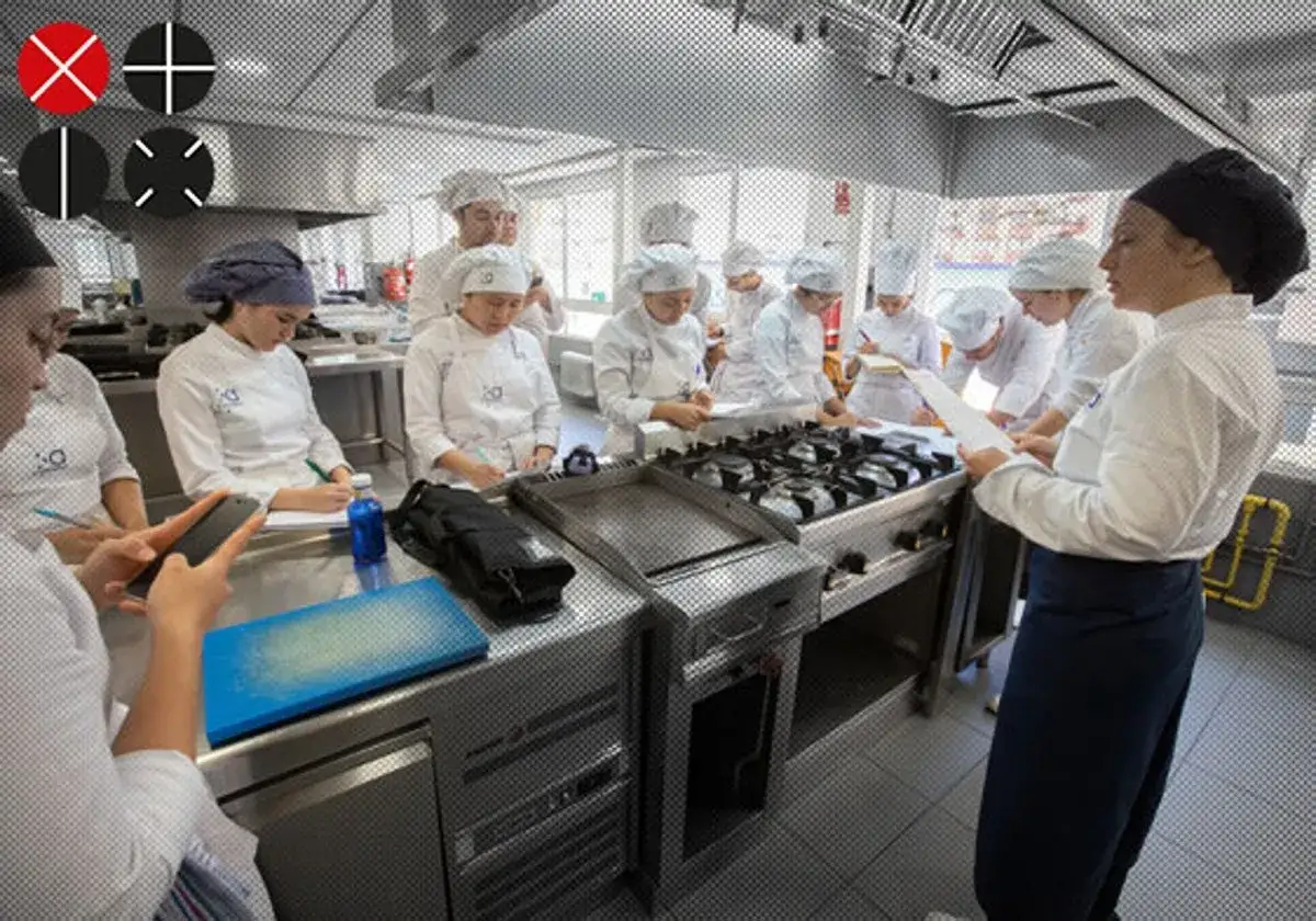 Estudiantes en un centro culinario mediterráneo, aprendiendo y tomando notas en una cocina profesional.