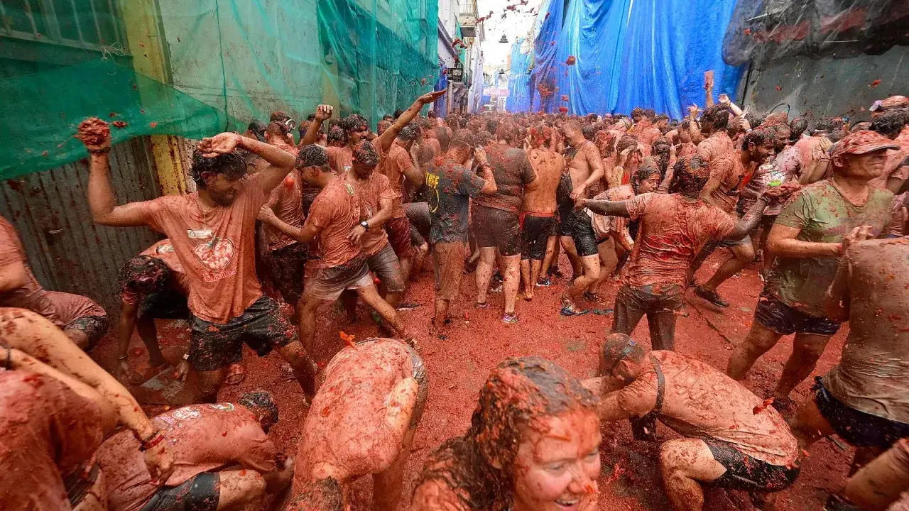 Multitud cubierta de tomate en la Tomatina, lanzando y jugando entre sí en una calle.