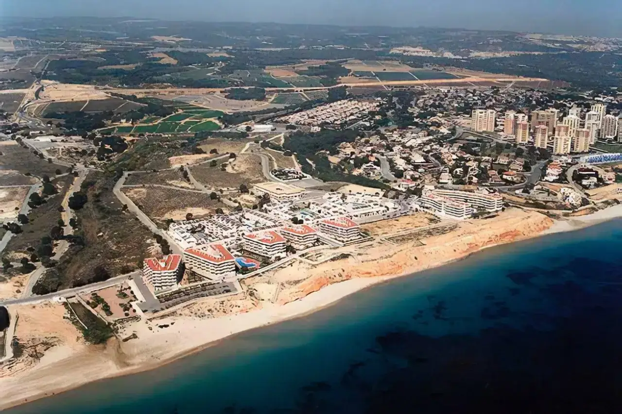 Vista aérea de una playa de mil palmeras con complejos residenciales modernos y el mar azul.