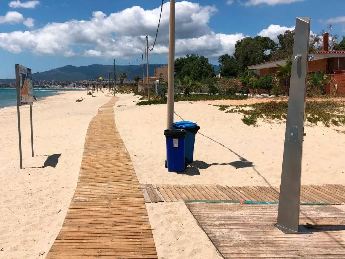 Pasarela de madera hacia el mar en playas con duchas en Alicante. Papeleras azules y ducha metálica a la derecha.