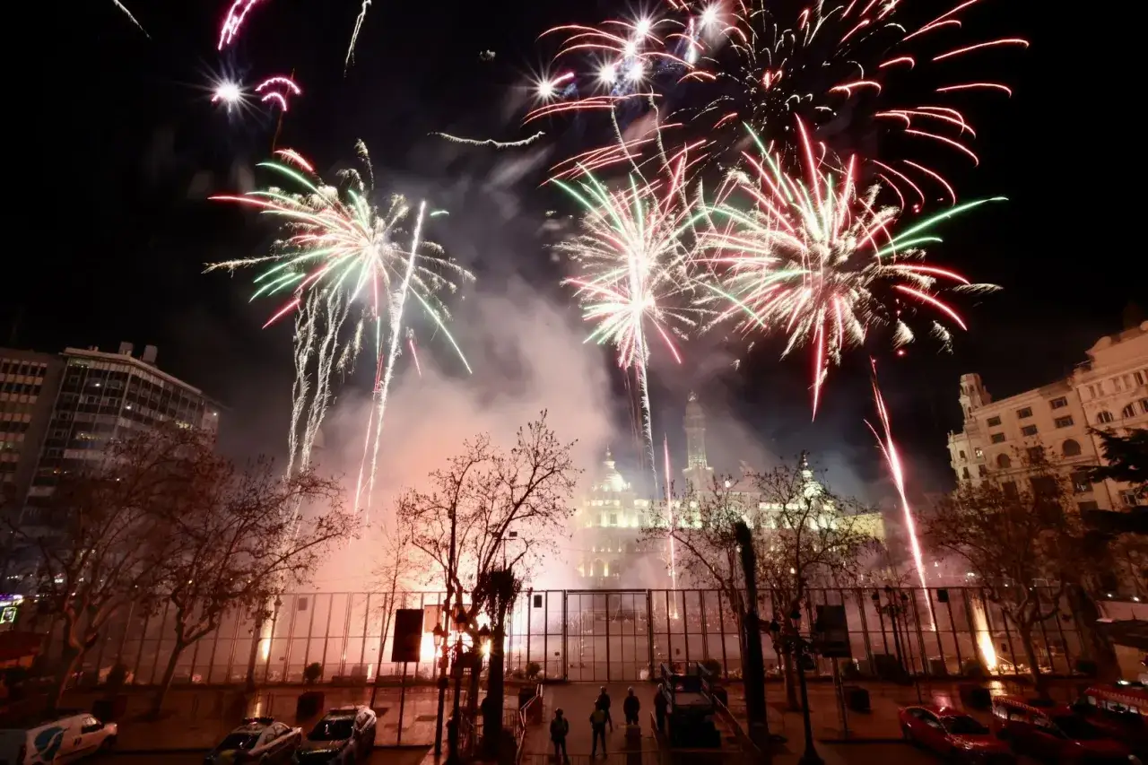 Espectacular fiesta en Valencia con fuegos artificiales iluminando el cielo nocturno sobre edificios históricos y árboles desnudos.