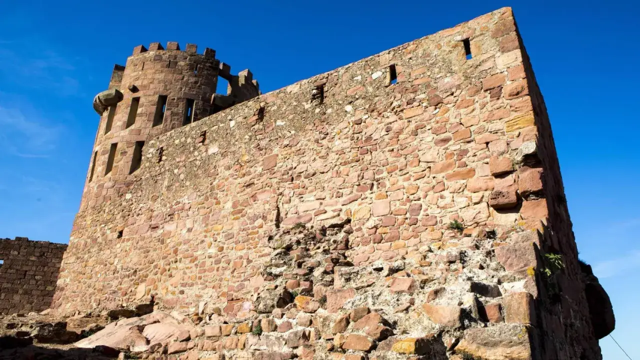 El imponente castillo de Villamalefa se alza contra un cielo azul intenso, sus muros de piedra rojiza testigos de historias pasadas.