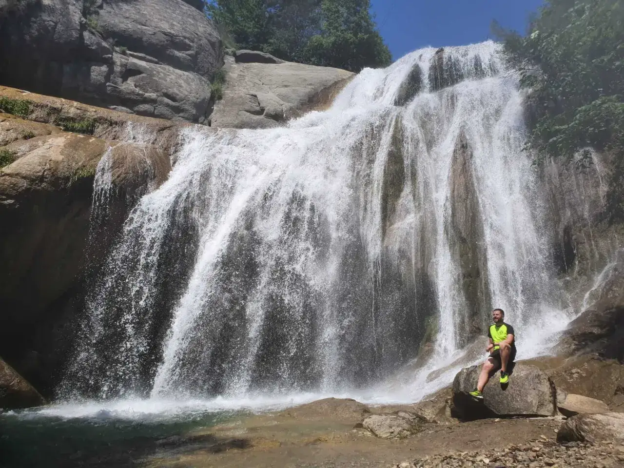 Hombre sentado en una roca frente al impresionante salt del moli, disfrutando de la fuerza del agua.
