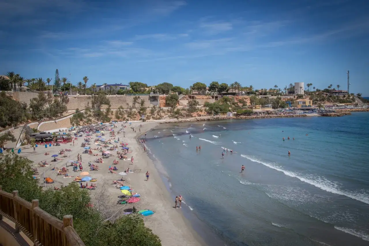 Gente disfrutando de un día soleado en una de las mejores playas de Cabo Roig. Arena dorada, aguas cristalinas y sombrillas por doquier.