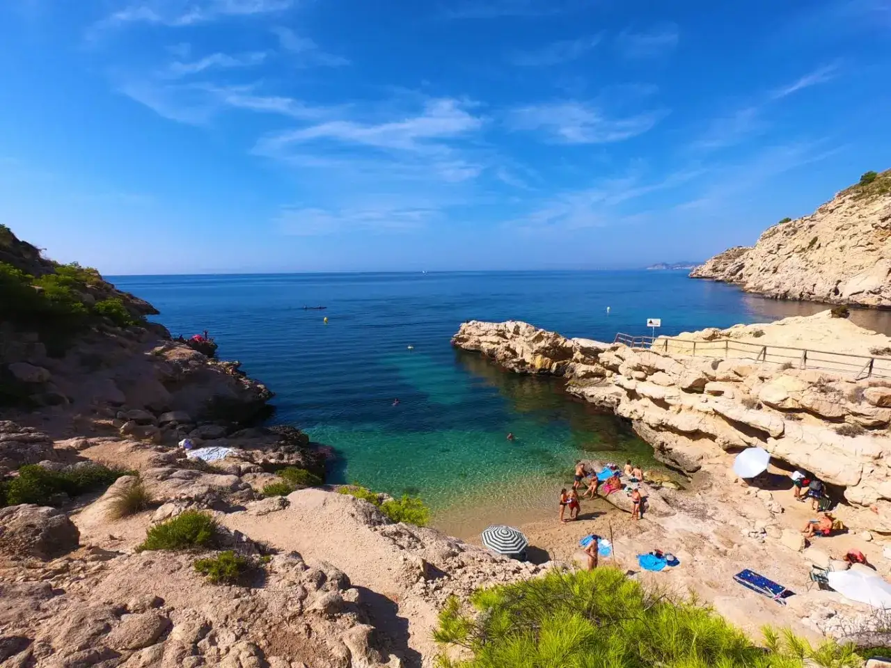 Un día soleado en el racó del conill, con aguas cristalinas y gente disfrutando de la playa rocosa.