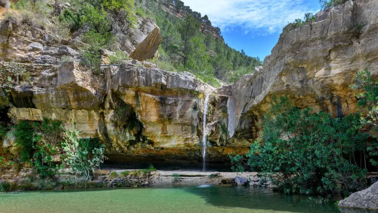 Cascada cayendo en un estanque de aguas cristalinas, rodeado de rocas y vegetaci&oacute;n exuberante. Un lugar id&iacute;lico para disfrutar de los charcos de quesa.