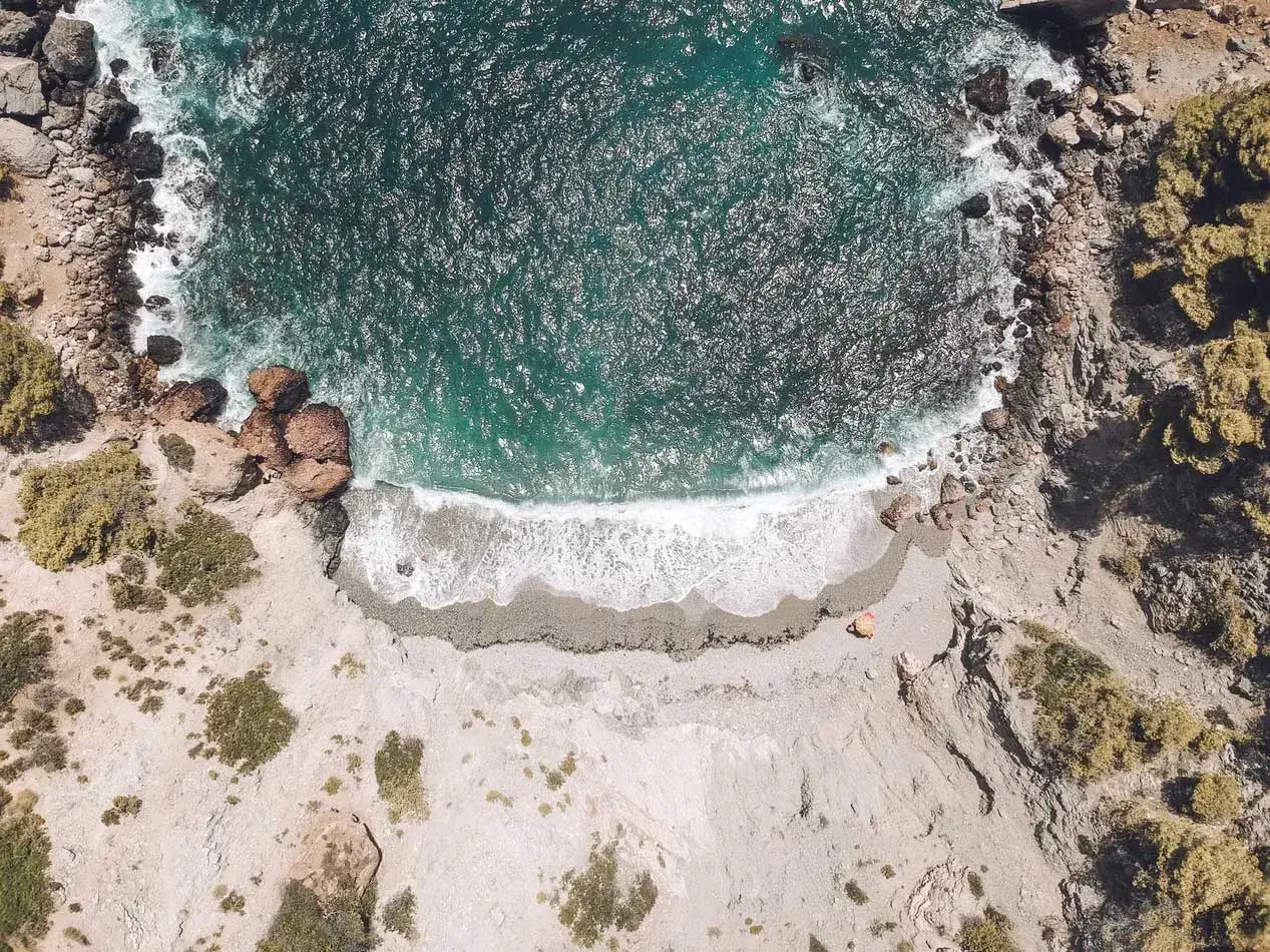 Vista aérea de una cala rocosa en la Costa Blanca España. El mar turquesa choca contra las rocas y la arena.