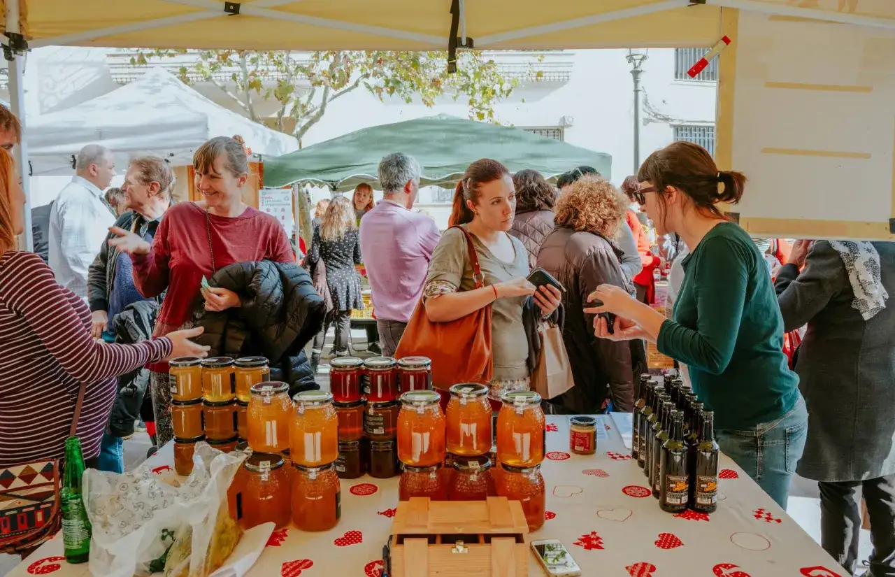Gente comprando miel y otros productos en un animado mercadillo en Elche.