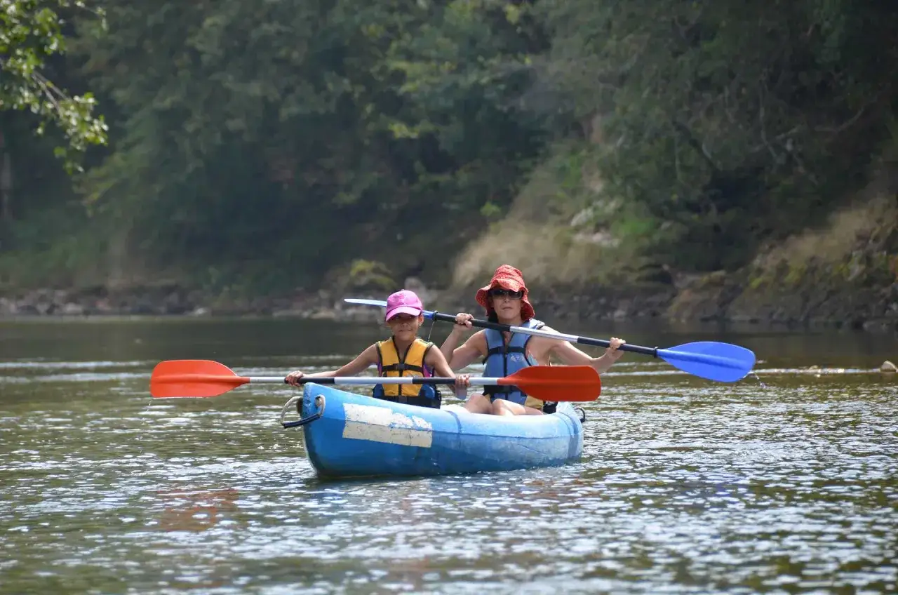 Dos chicas disfrutan de un paseo en canoa en el campamento La Serrana, remando juntas por un río tranquilo rodeado de vegetación.