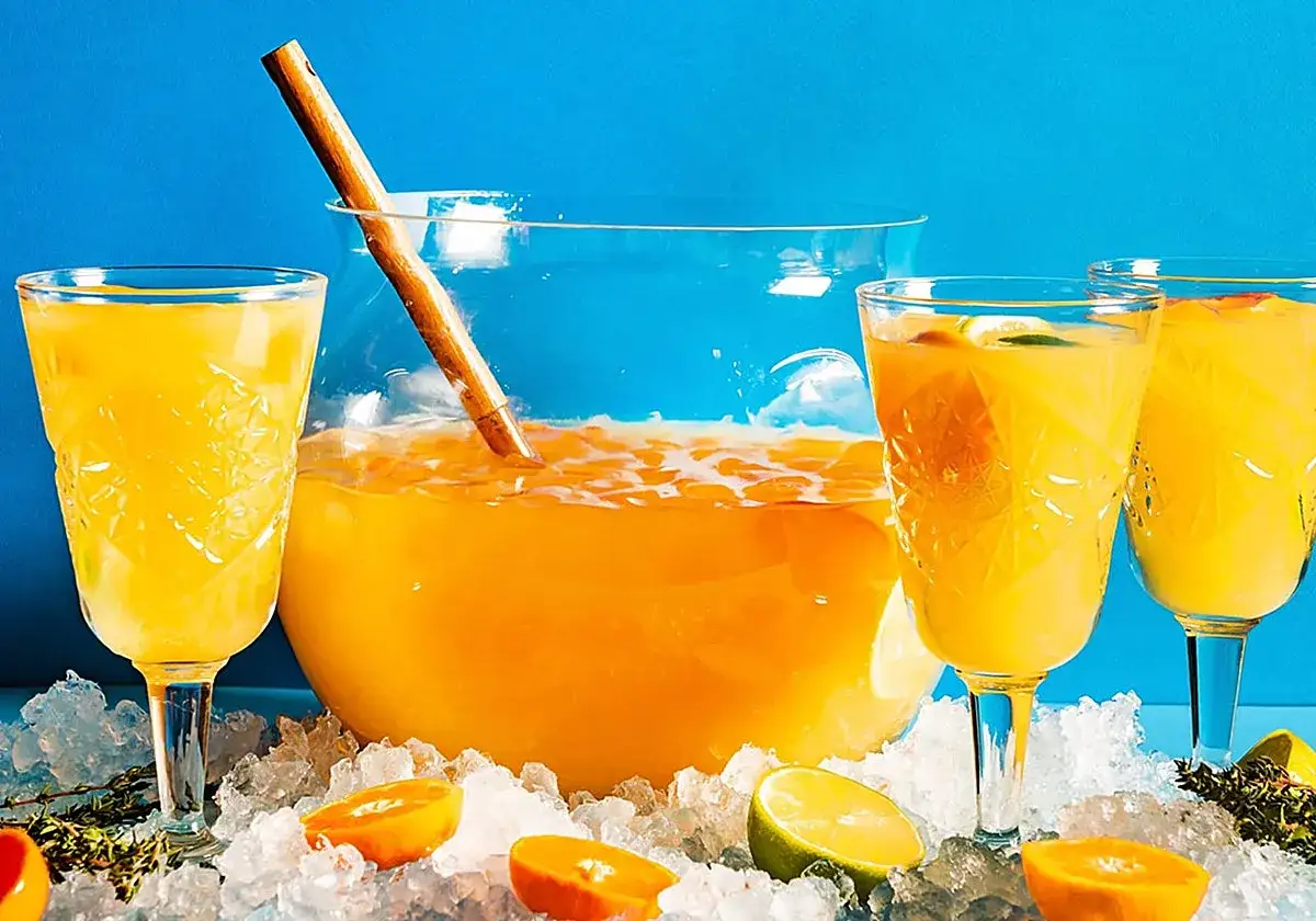 Un refrescante agua de valencia servida en copas y ponchera, rodeada de hielo, rodajas de naranja y lima.