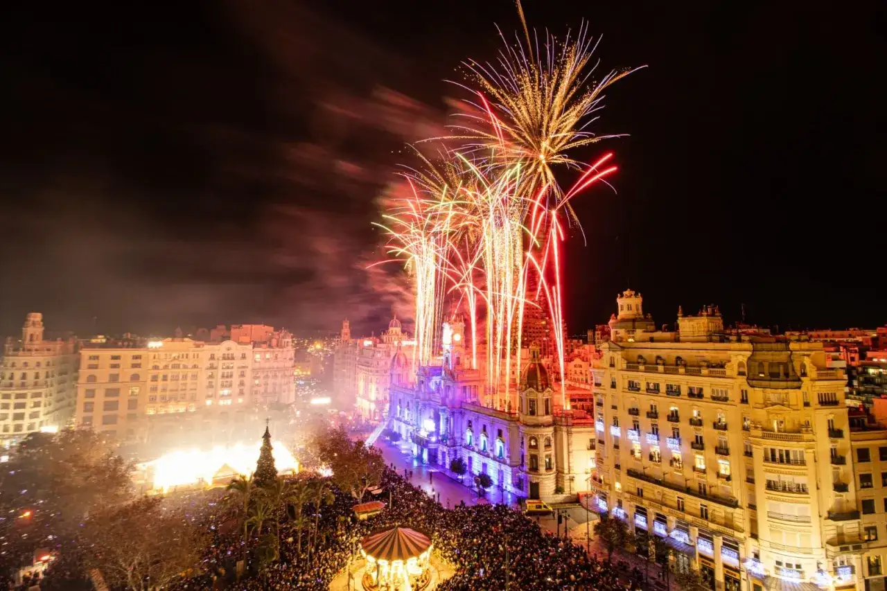 Espectacular noche de fuegos artificiales sobre el ayuntamiento de Valencia. La multitud celebra bajo el cielo iluminado.
