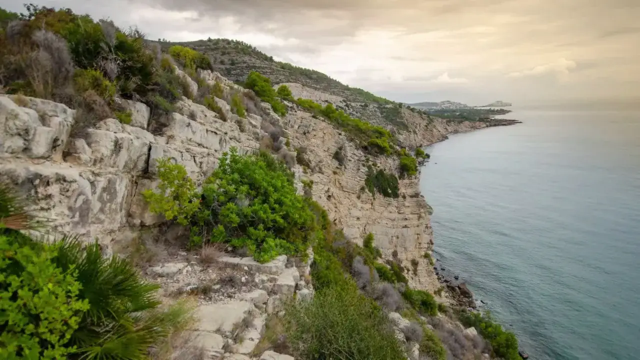 Acantilados rocosos y vegetación agreste en la sierra de Irta, con el mar Mediterráneo extendiéndose hacia el horizonte bajo un cielo nublado.