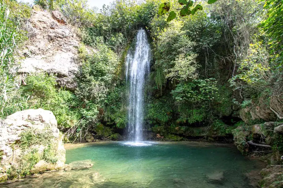 Los chorradores de Navarres, una cascada cae en una poza de agua turquesa rodeada de vegetación exuberante y rocas.