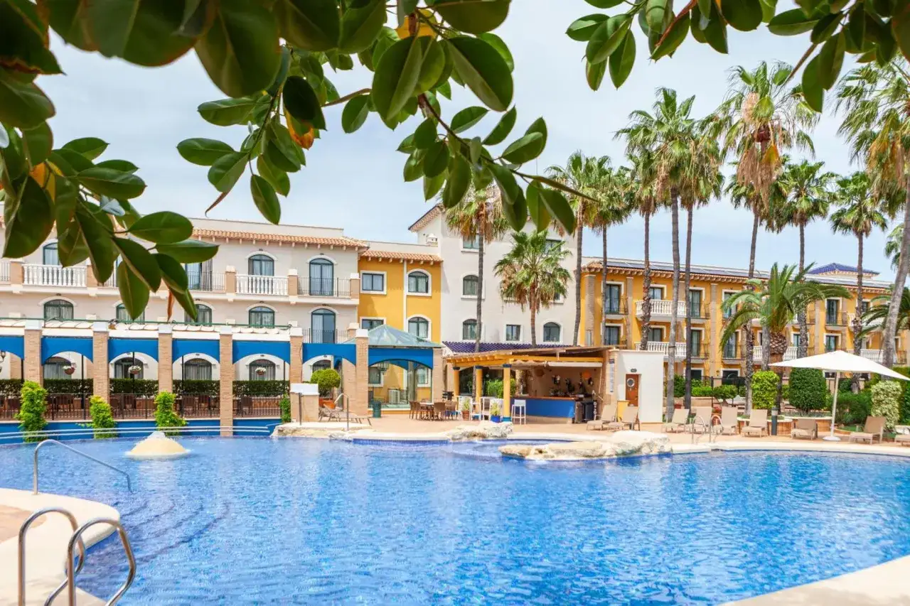 Piscina azul cristalina frente a un hotel con palmeras. El hotel la laguna spa & golf ofrece un bar junto a la piscina y áreas de descanso.