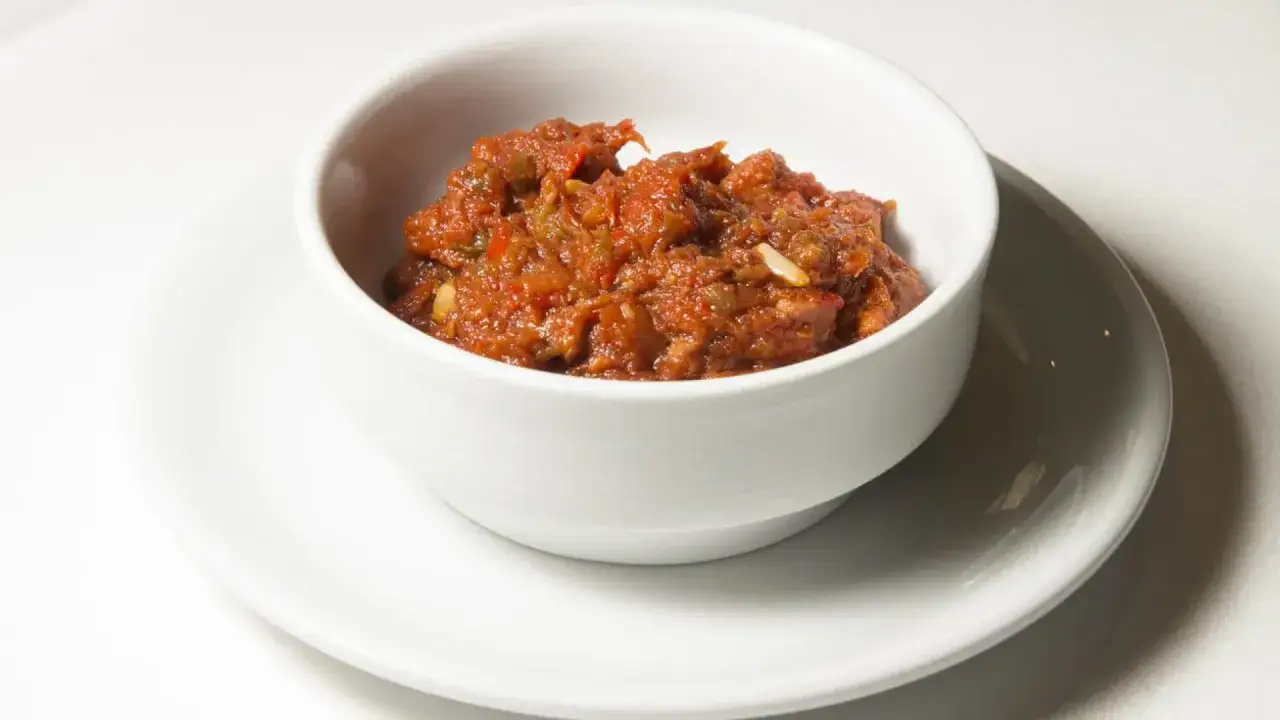 Un cuenco blanco contiene una sabrosa salsa de tomate y pimientos, ideal para saber qué comer en Valencia.