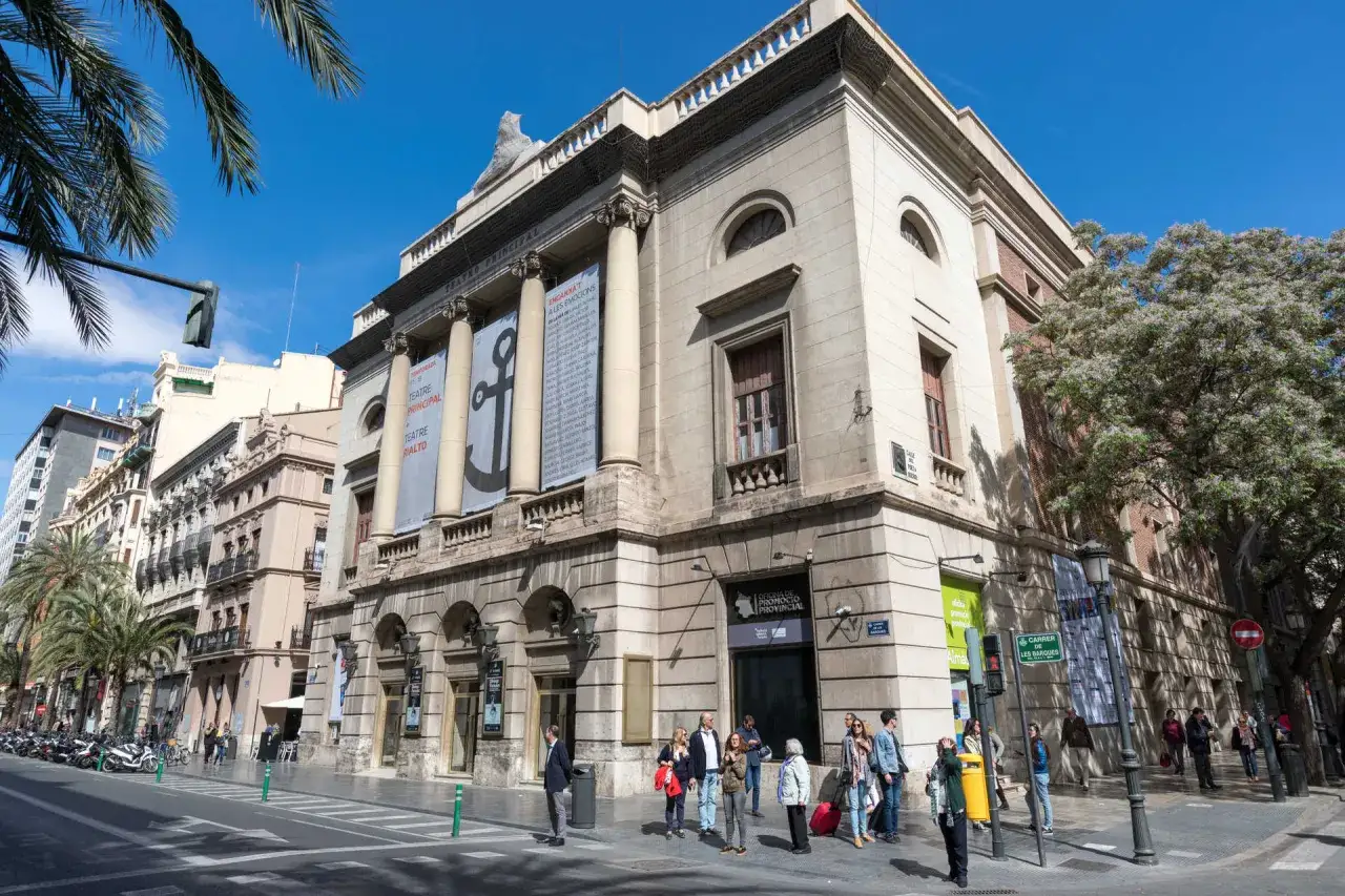 El teatro en Valencia, el Principal, con su fachada clásica y carteles anunciando espectáculos, se alza majestuoso bajo un cielo azul.