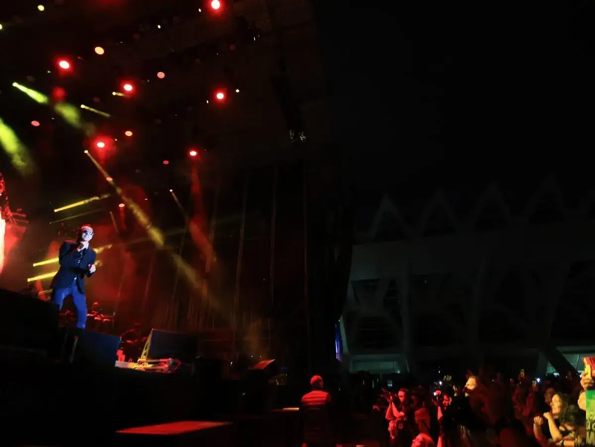 Marc Anthony canta en un espectacular concierto de Valencia, iluminado por luces rojas y amarillas. La multitud disfruta de la música.