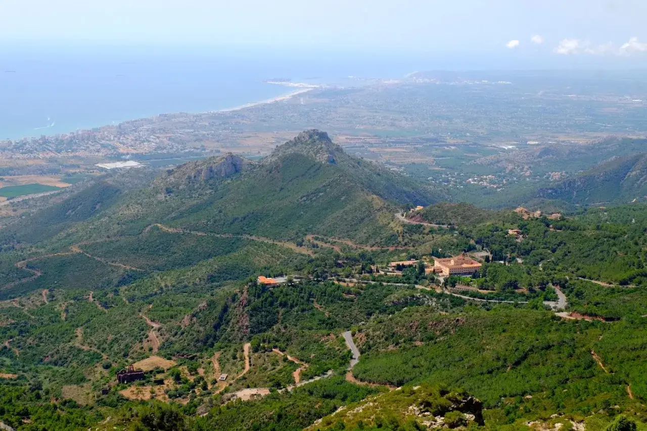 Vista panorámica del Desert de les Palmes, con el mar Mediterráneo al fondo y edificios históricos entre la vegetación.