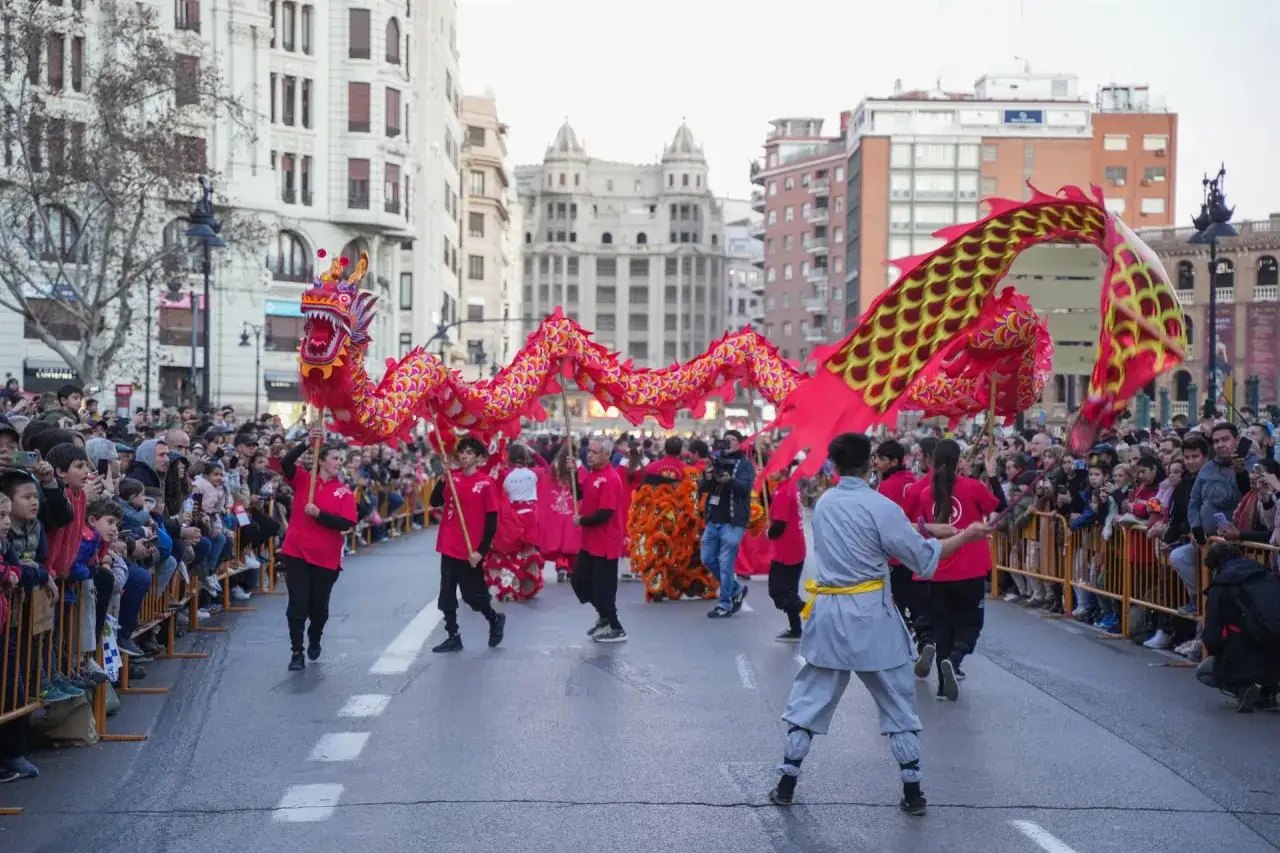 Dragón rojo y dorado baila en la calle durante la celebración del año nuevo chino en Valencia, ante una multitud expectante.