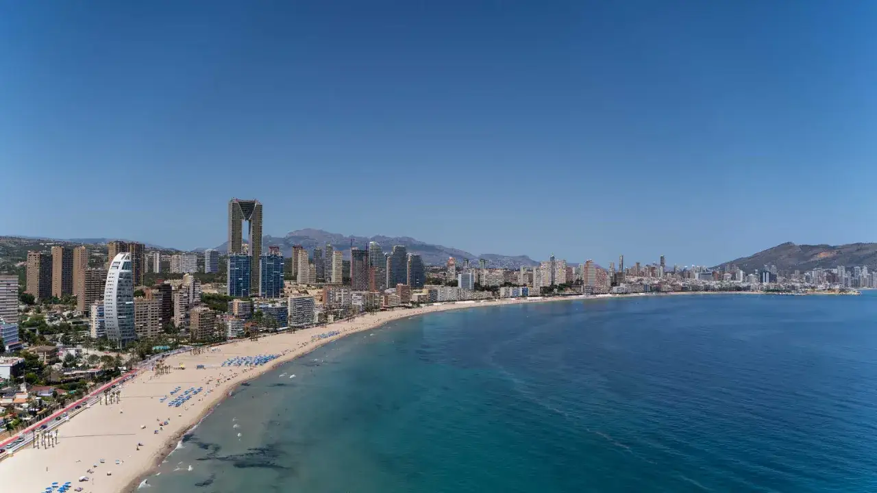 Amplia vista de la playa Poniente en Benidorm, con su arena dorada, aguas turquesas y un horizonte de rascacielos.