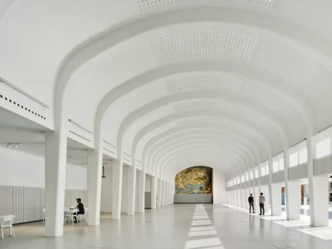 Interior moderno y luminoso del espacio Seneca Alicante, con arcos blancos y un mural al fondo.