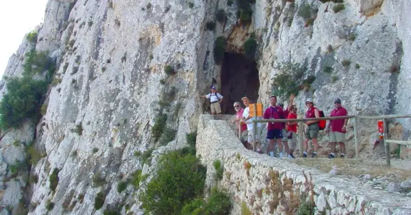 Grupo de excursionistas en el sendero del Peñón de Calpe, con una cueva a la izquierda y vistas rocosas.